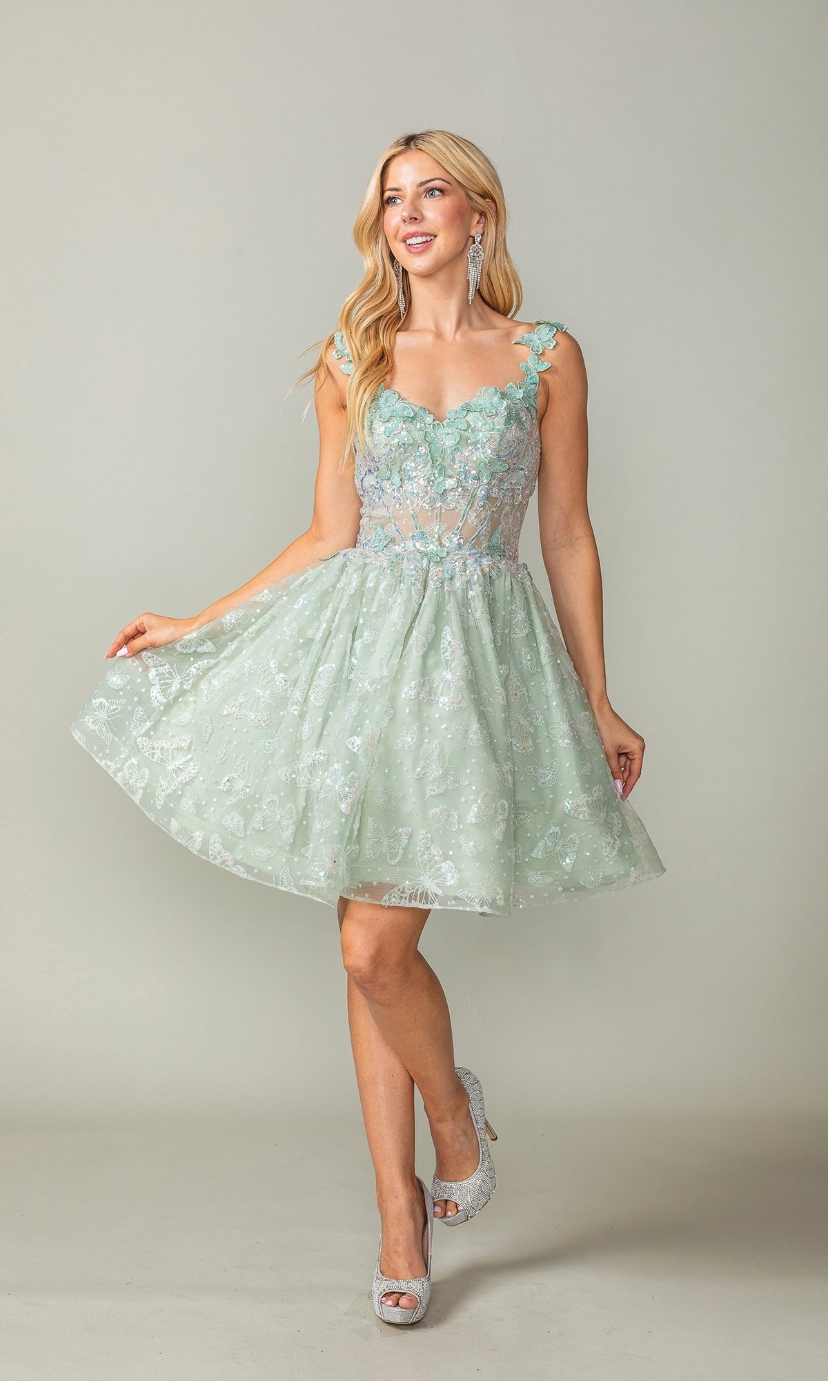 A woman wears the Sparkly Short Butterfly Homecoming Dress 3361—a light green, knee-length, sleeveless A-line dress with floral lace accents and silver heels—posing against a plain background.
